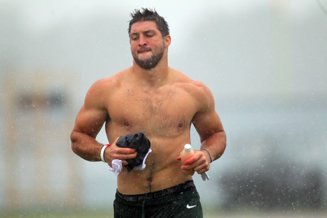 Tim Tebow runs off the field shirtless during a New York Jets field practice at training camp, in the rain.