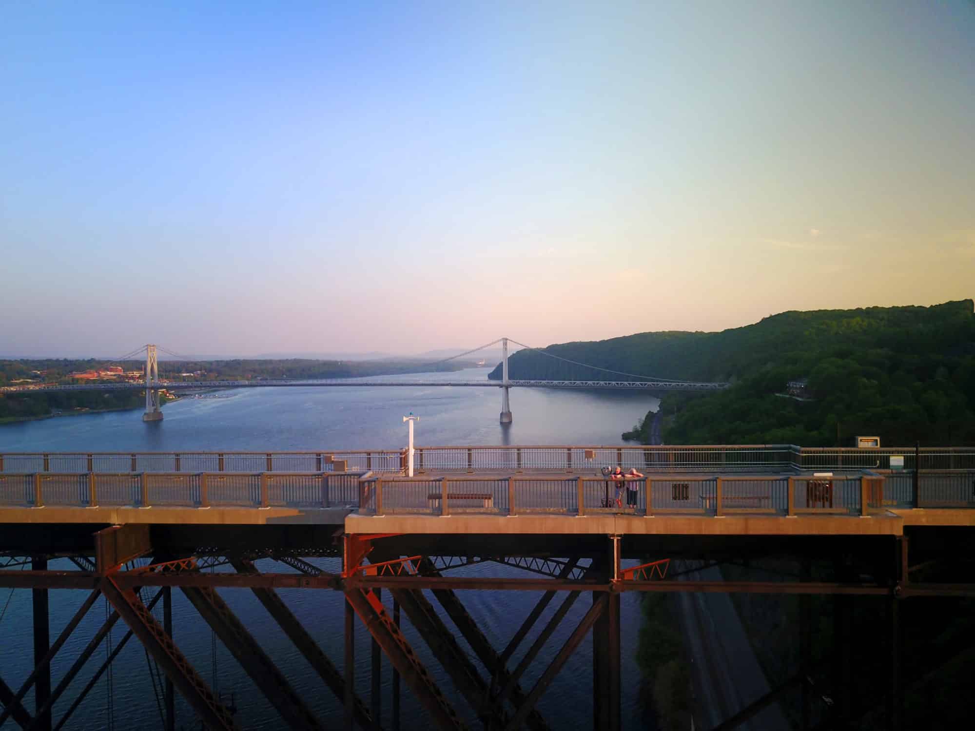 An aerial view of the tourist attraction Walkway Over the Hudson in Poughkeepsie, New York, at sundown dusk. Picture shows blue water of Hudson River, the Hudson Highlands beyond, and visitors. Suzy Allman photo.